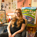 Photograph of Chloe smiling whilst leaning back in a chair with art in the background, she has long blonde hair and is wearing all black